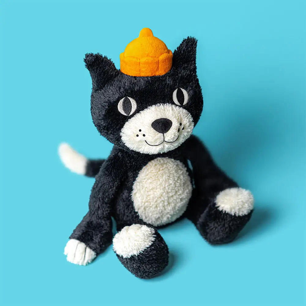 A JellyCat plush toy of a black and white cat wearing a cheerful yellow hat, showcasing its charming design and appeal.